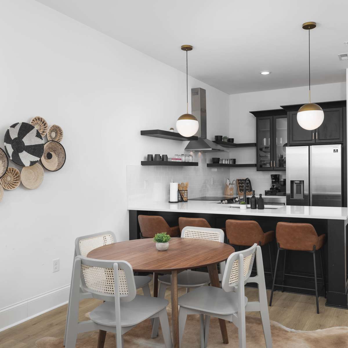 A modern kitchen with black cabinets and stainless steel appliances is connected to a dining area featuring a round wooden table and gray chairs.