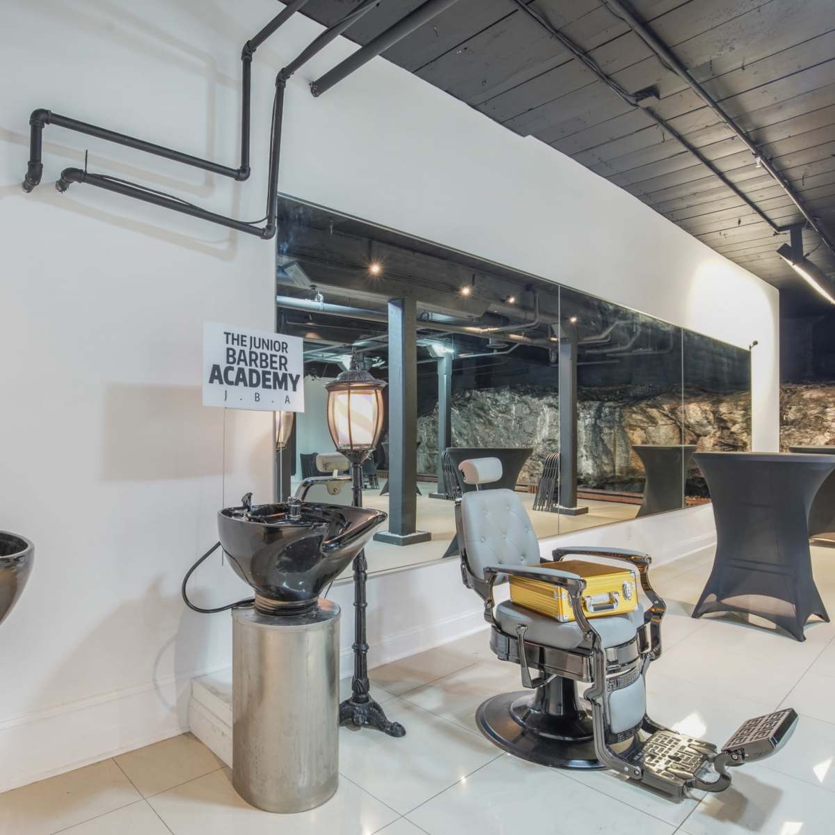 A modern barber shop interior featuring a barber chair, washbasins, and a wall-mounted sign for "The Under Barber Academy."