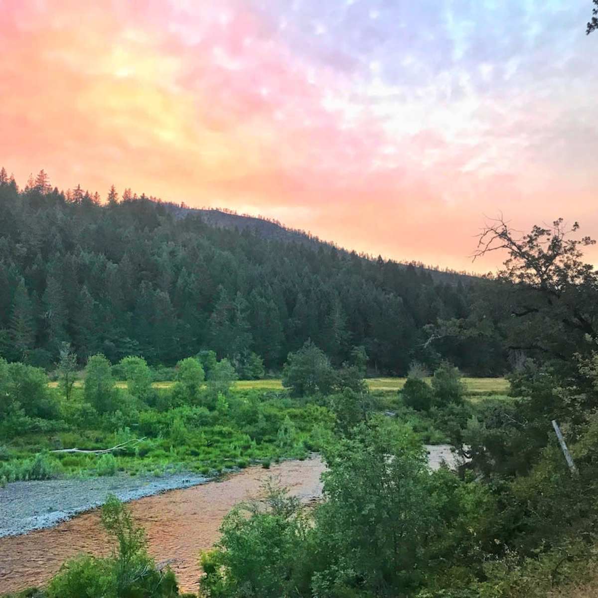 A river flows through a forested landscape under a colorful sky at dusk.