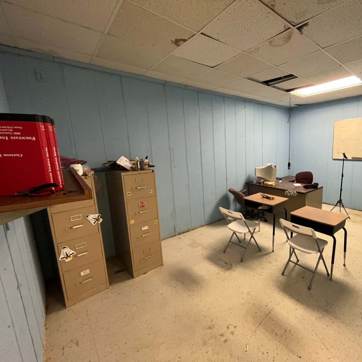 A small, empty room with blue walls, a table and chairs, a whiteboard, and file cabinets.