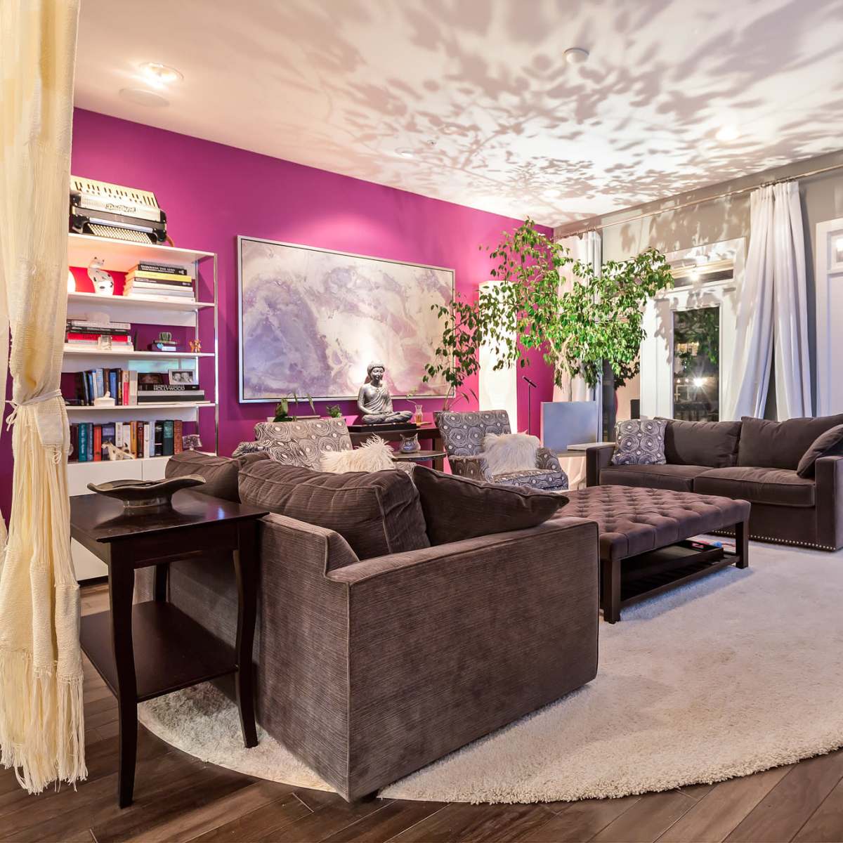 The living room features a circular rug surrounded by gray sofas, a coffee table, and a large potted plant, with a purple accent wall and glass doors leading outside.