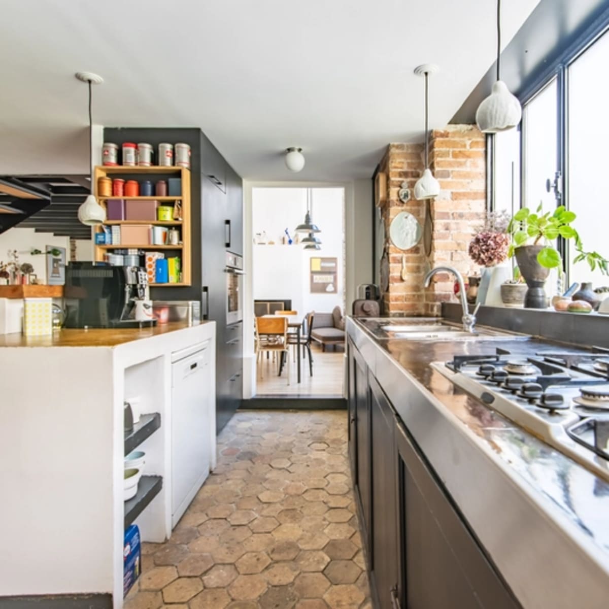 A modern kitchen features a central island with a gas stove, large windows providing natural light, and a view of a dining area.