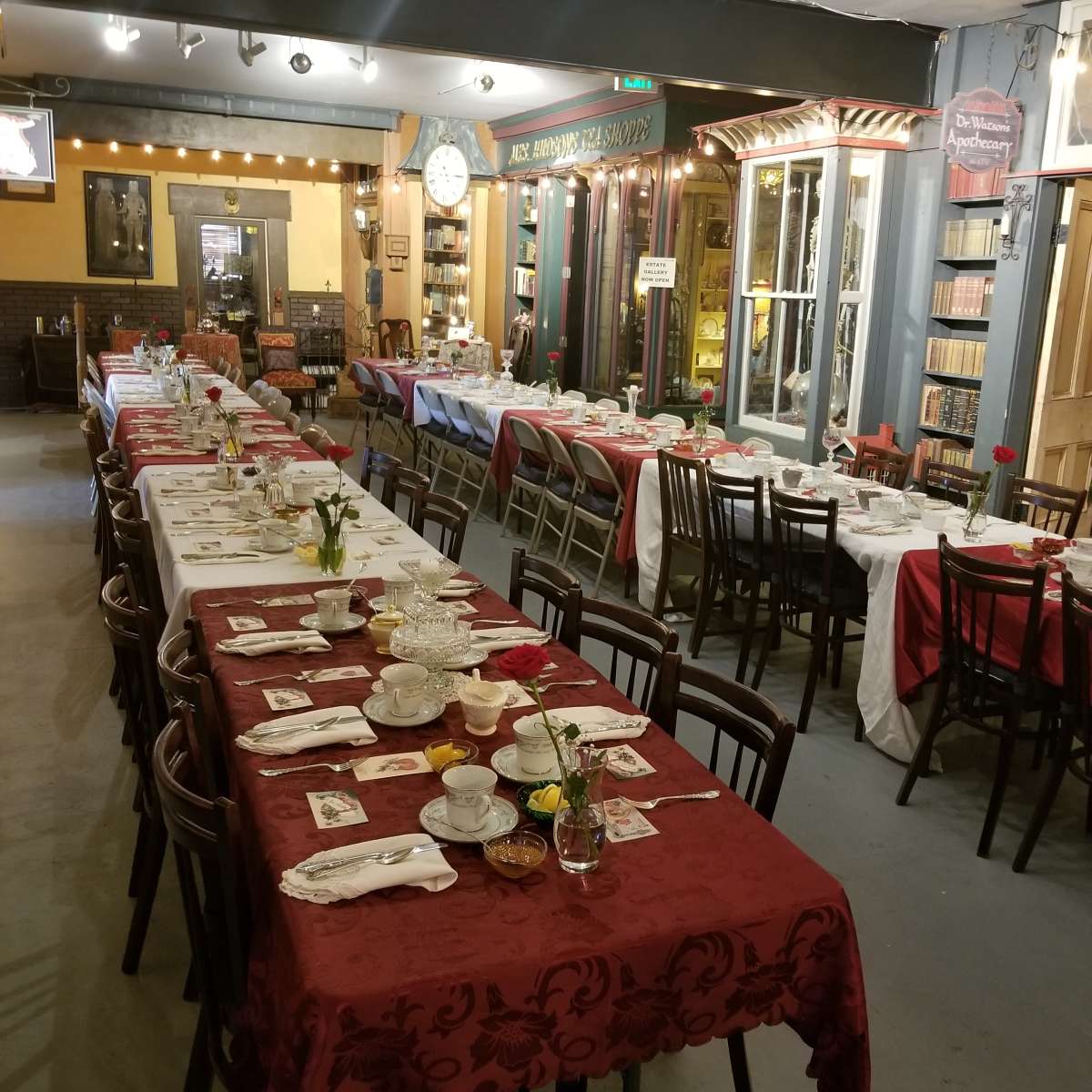A dining area arranged with long tables covered in red and white tablecloths, set for a meal with dishes, utensils, and small flower centerpieces.