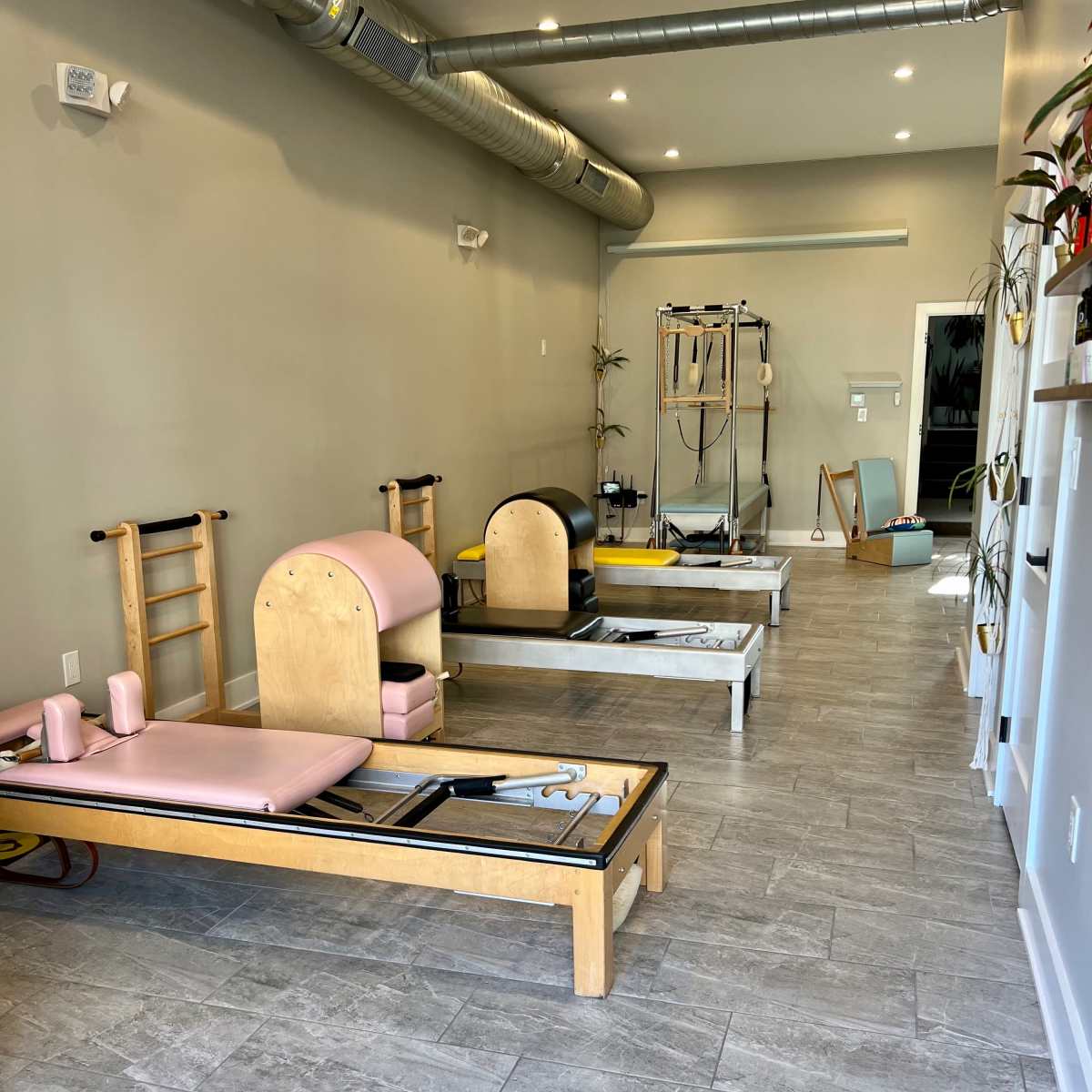 A modern Pilates studio featuring several reformer machines arranged along a spacious, light-colored floor with muted walls and overhead lighting.