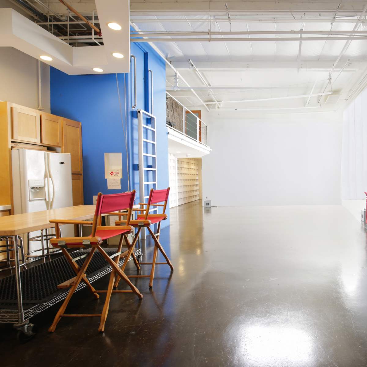 A spacious, open studio with a kitchen area on the left and a blank wall on the right.
