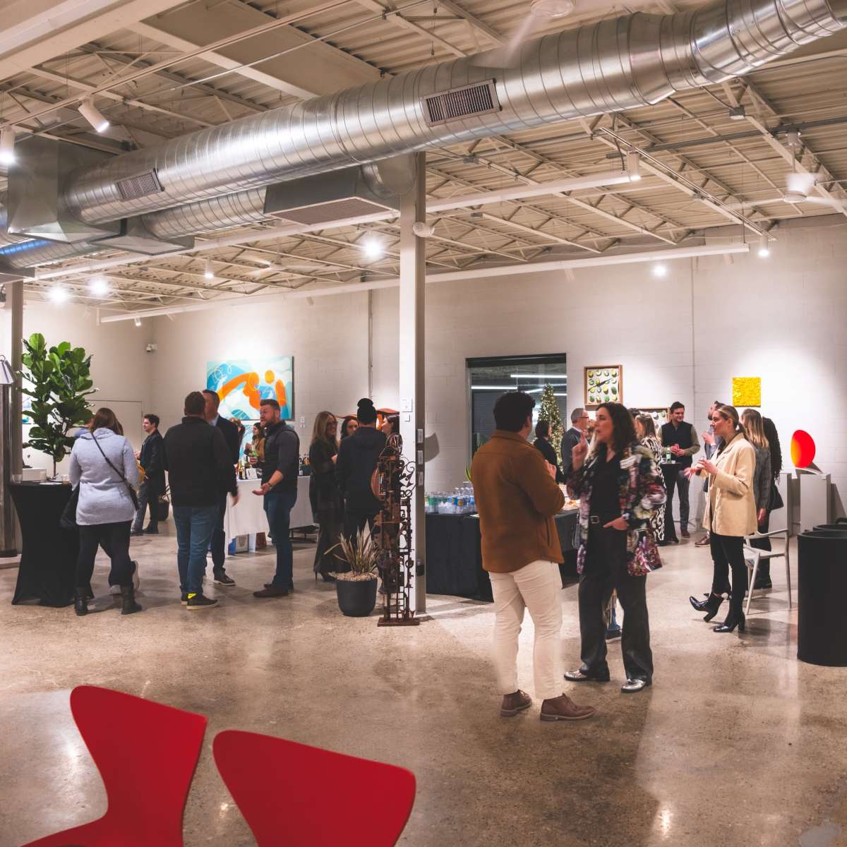 A gathering of people is taking place in a spacious art gallery with various artworks displayed on the walls.