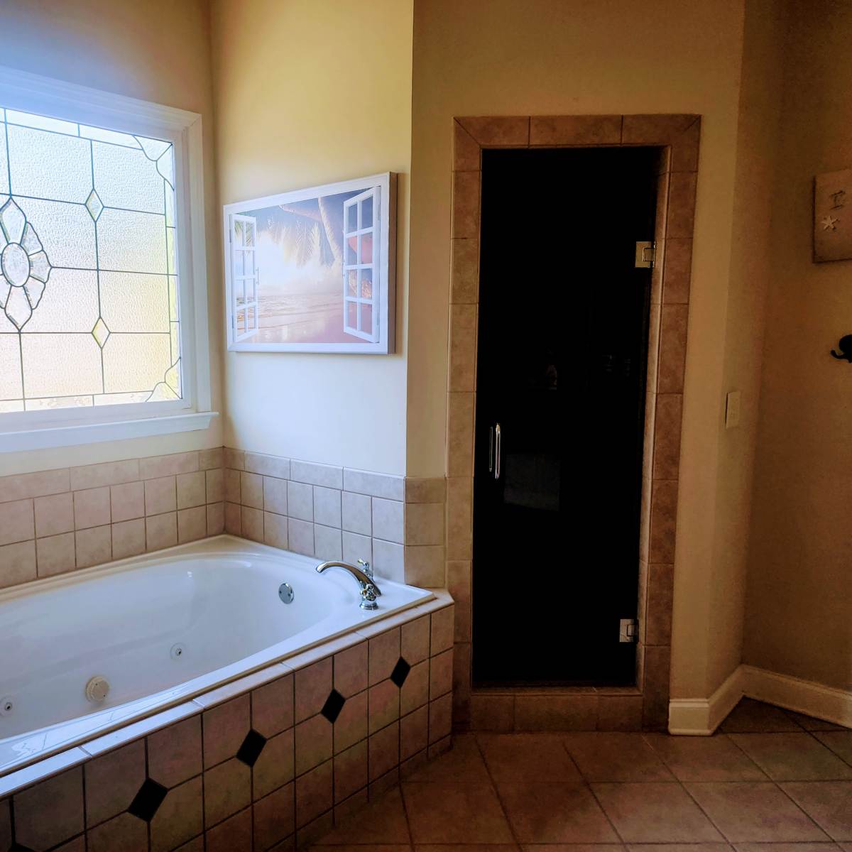 A bathroom featuring a white jetted bathtub next to a glass-enclosed shower and a decorative window.