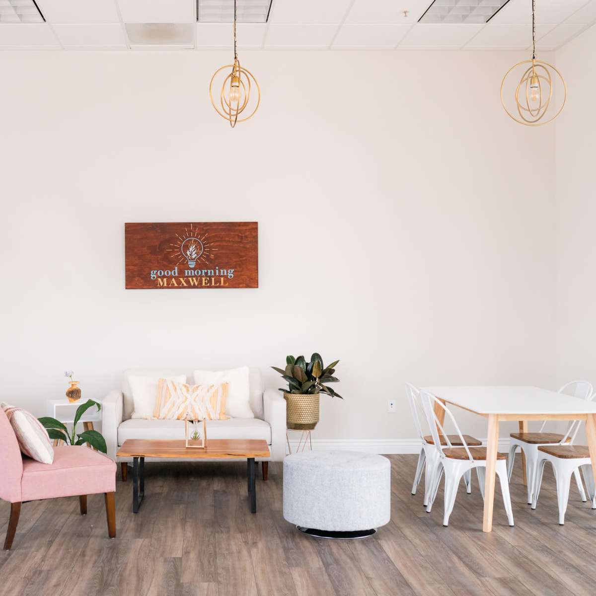 A bright, minimalist interior with a seating area, a wooden table, and two smaller tables arranged in a well-lit space.