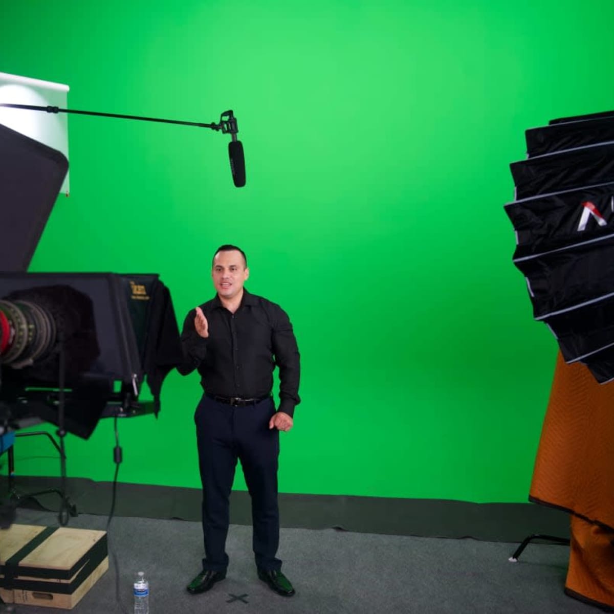 A man stands in front of a green screen, gesturing while multiple cameras and lighting equipment surround him.