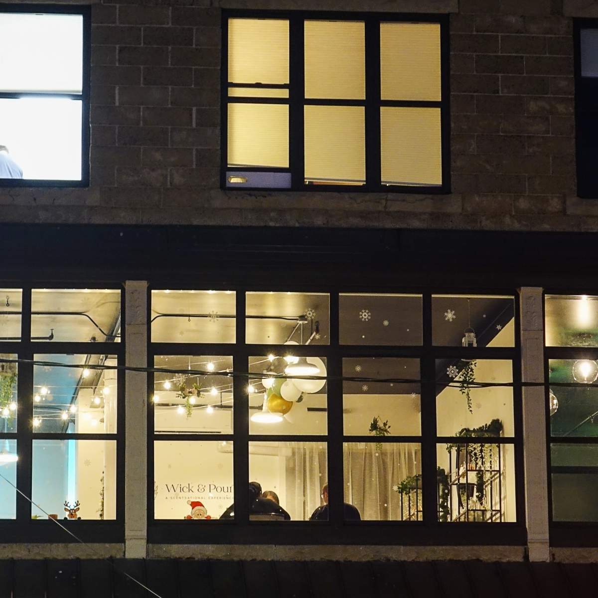 A brightly lit window of a café with patrons seated inside, observed from the outside at night.