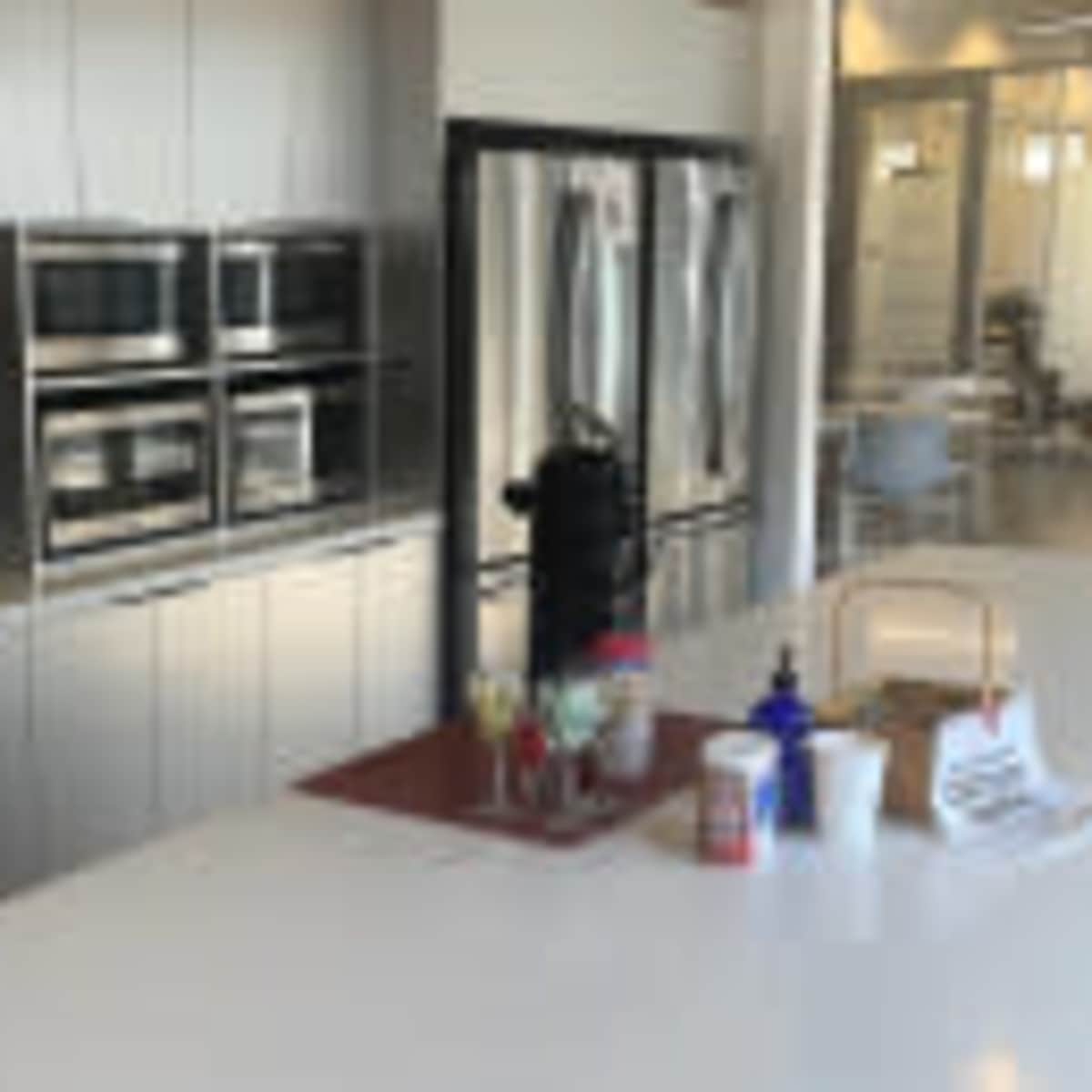 A modern kitchen with multiple stainless steel appliances, including two microwaves and three refrigerators, alongside a countertop featuring various containers and a coffee machine.