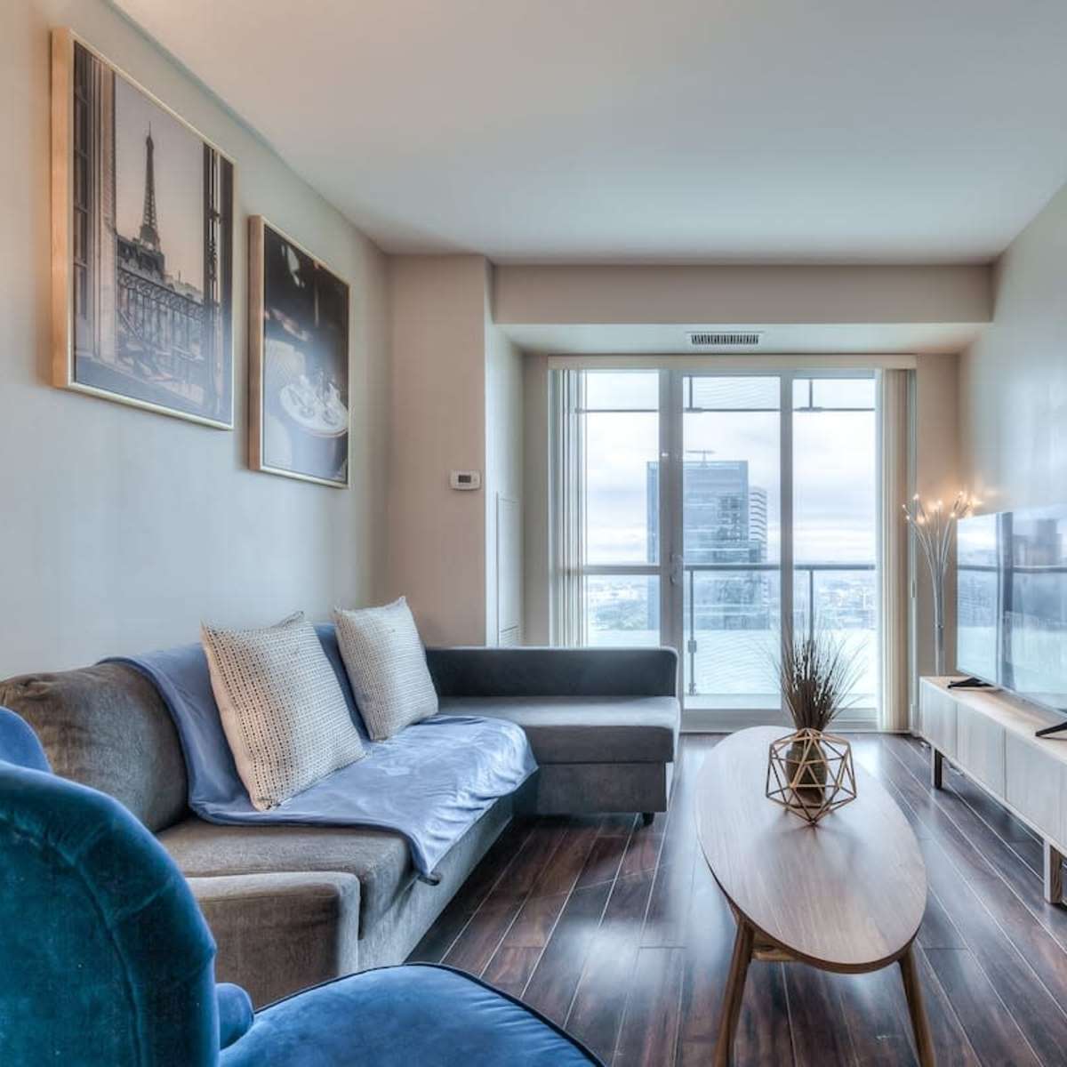 A modern living area with a sofa, coffee table, and a television, featuring large windows that offer a city view.