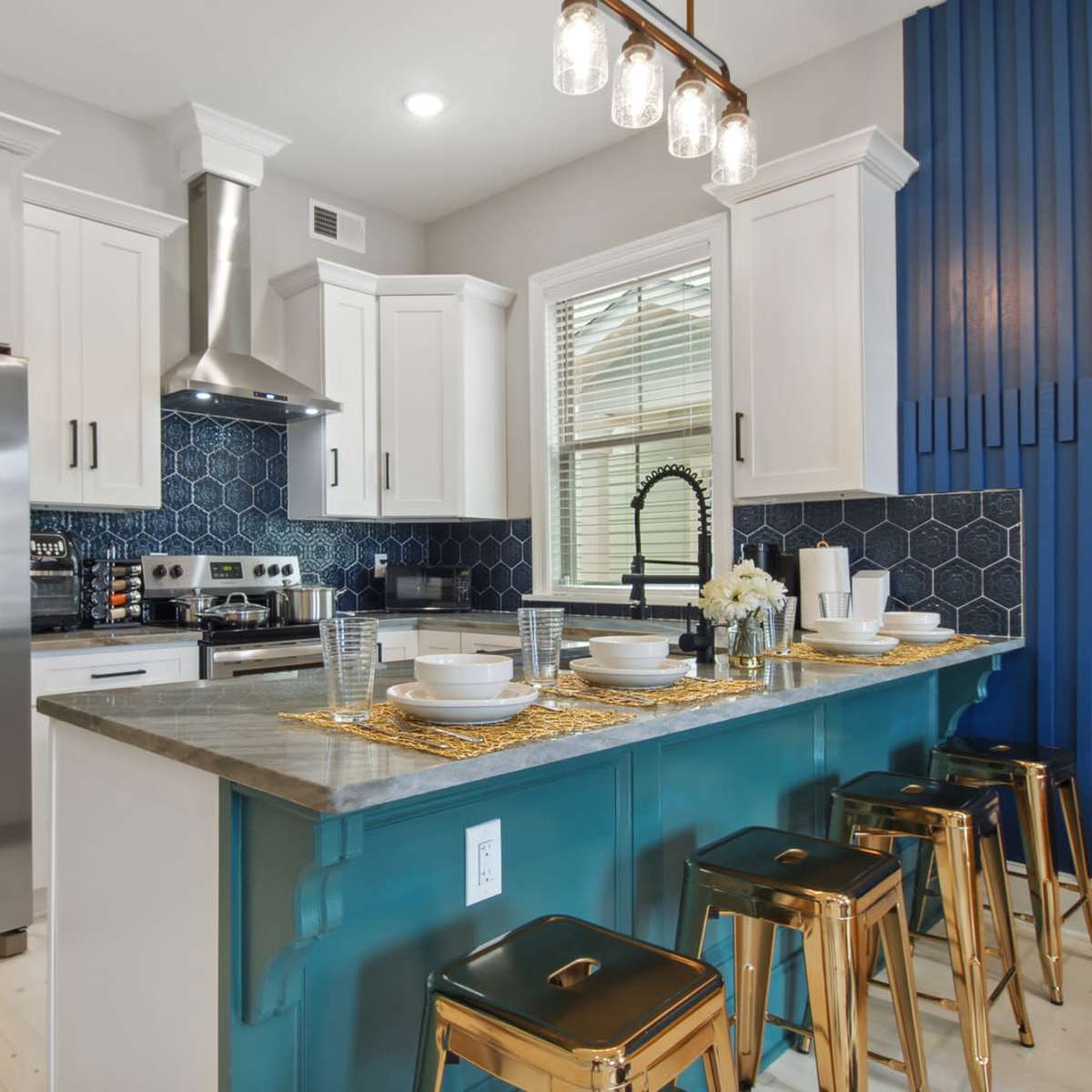 A modern kitchen features a central island with metallic bar stools, sleek cabinets, and a blue accent wall, complemented by geometric tile backsplash.