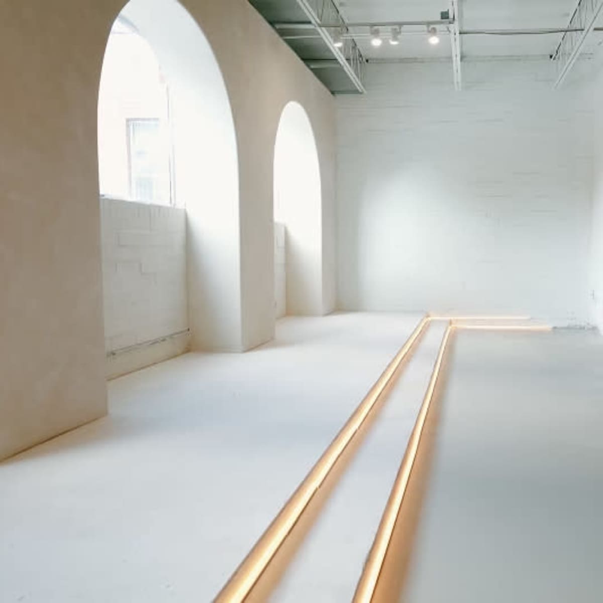 A minimalist interior space with arched windows and two illuminated lines on the floor.