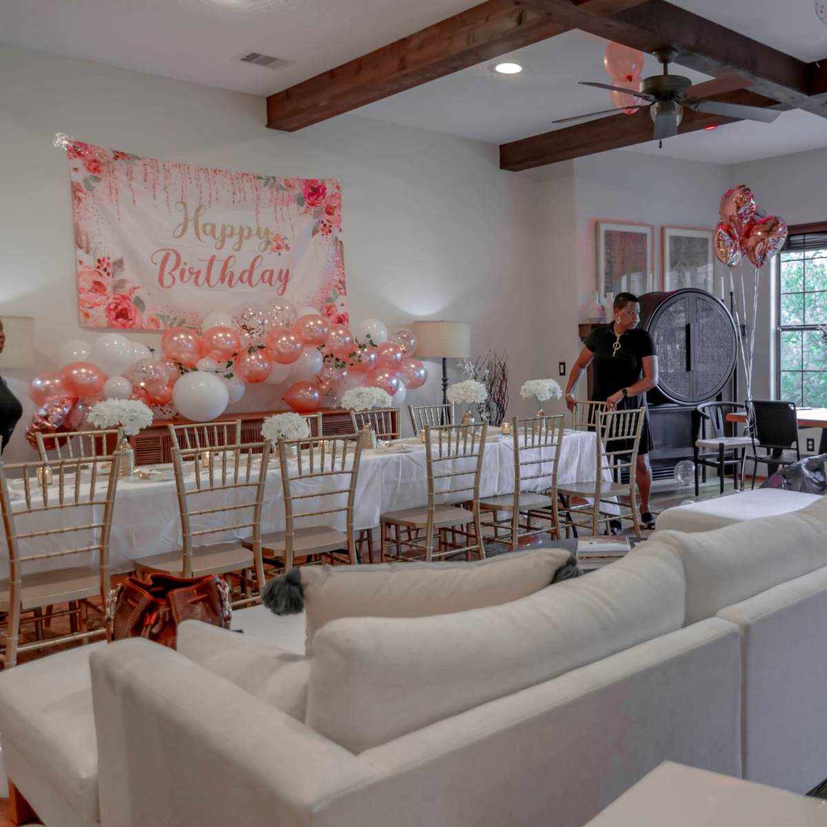 A dining area is decorated for a birthday celebration, featuring a banner, balloons, and a long table set with chairs.