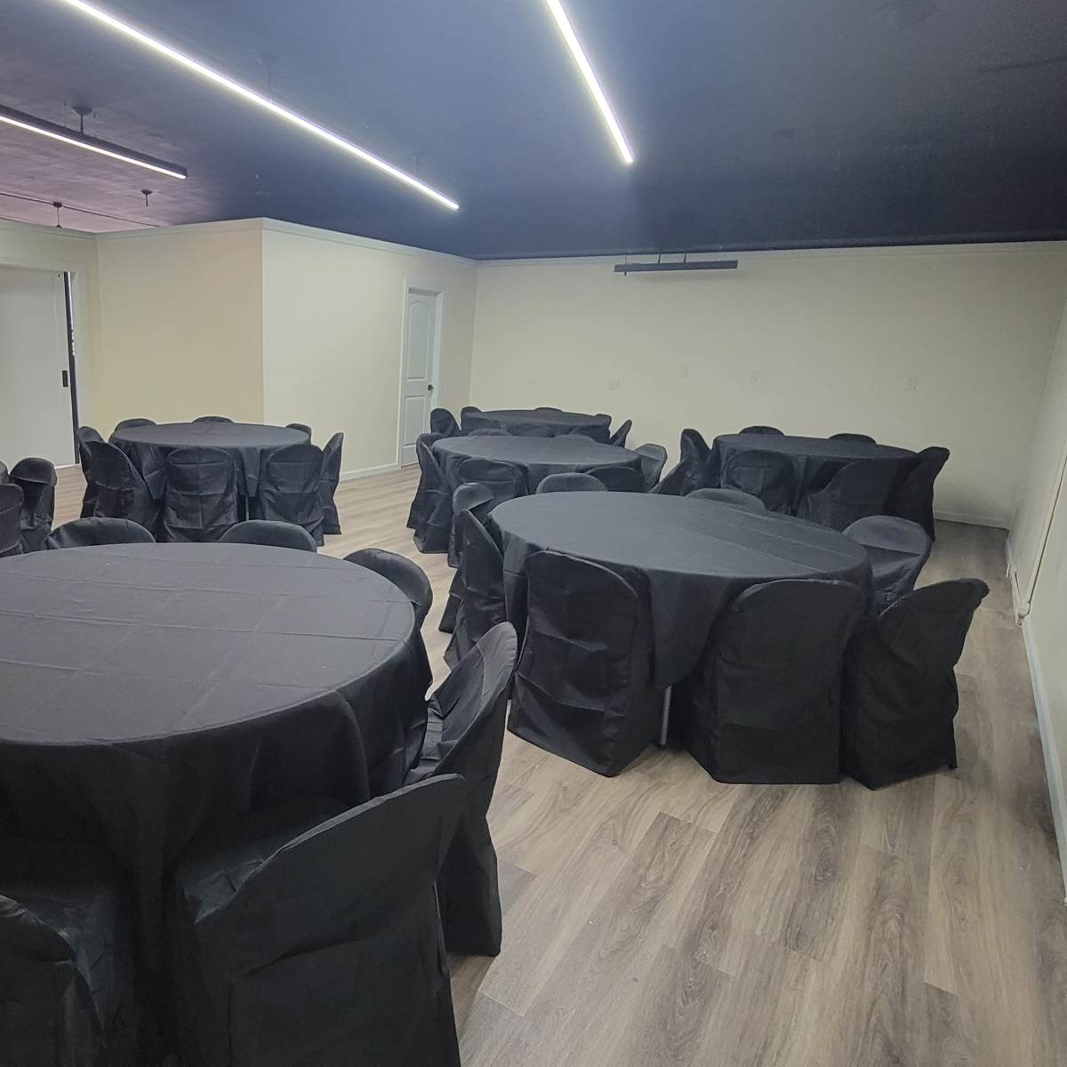 A spacious event room set with multiple round tables covered in black cloth and surrounded by matching chairs.