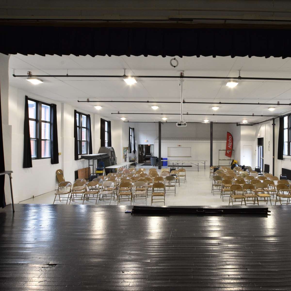 A spacious auditorium features rows of folding chairs set up for an event, with large windows allowing natural light to enter.