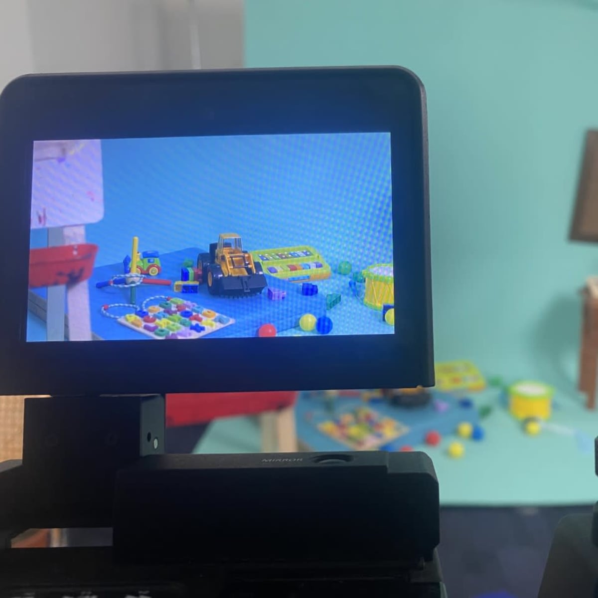 A camera viewfinder displaying a colorful arrangement of toys and play materials in a studio setup with a light blue background.