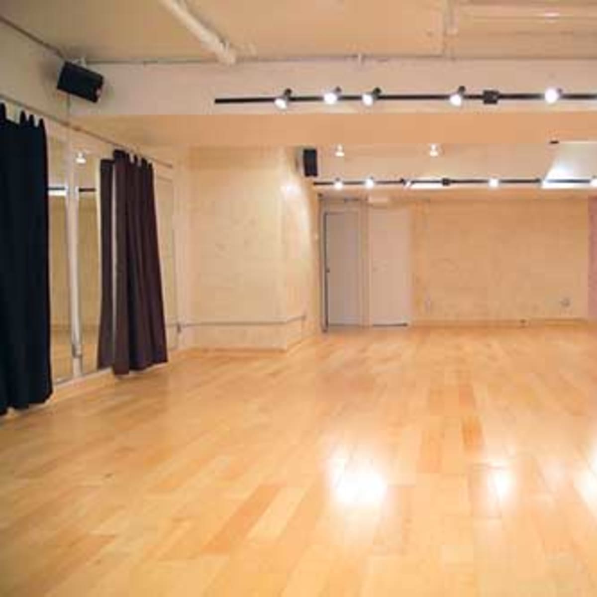 An empty dance studio with wooden flooring and muted wall colors, featuring mirrors and spotlights.