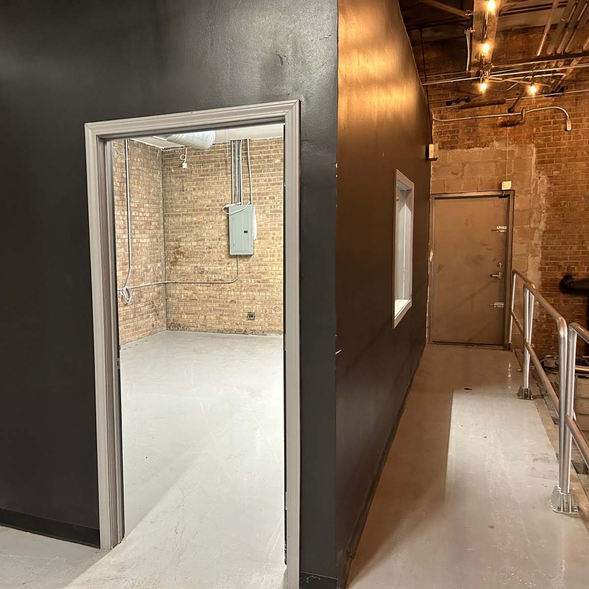A doorway leading from a black-painted wall into a room with exposed brick walls and a concrete floor.