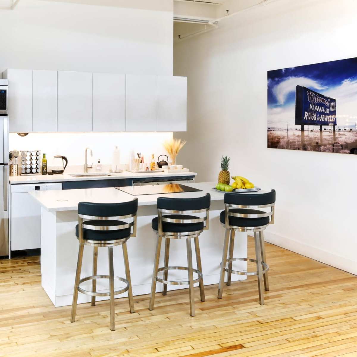 A modern kitchen featuring sleek cabinetry, stainless steel appliances, and three bar stools positioned at a kitchen island.