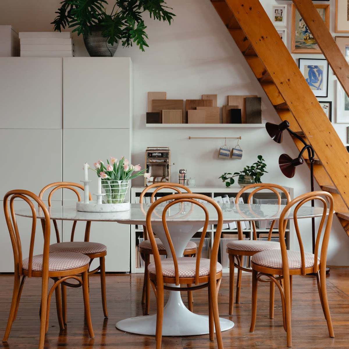 A stylish dining area features a round table with wooden chairs, surrounded by a mix of décor and artwork against a backdrop of wooden beams.