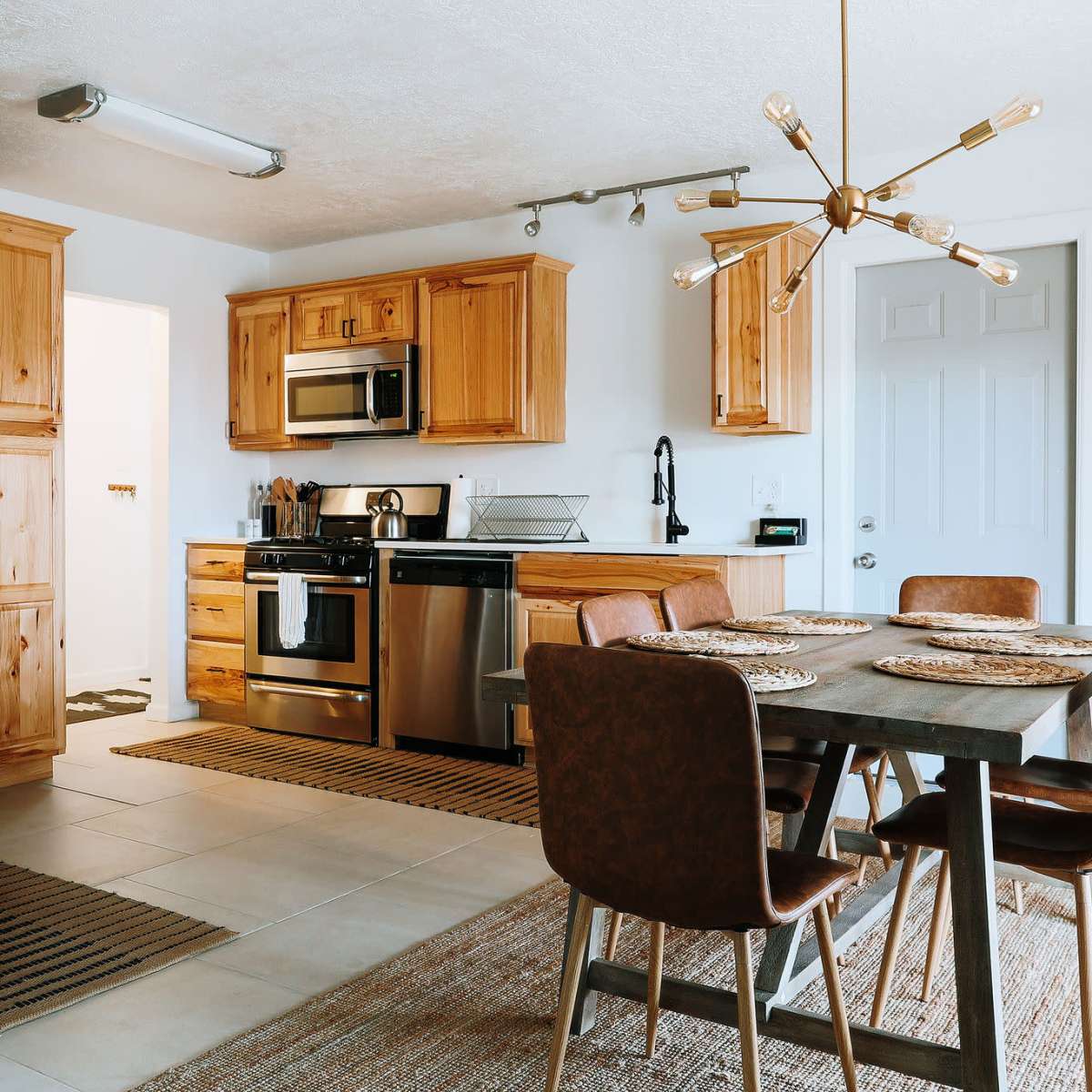 A modern kitchen with wooden cabinetry, stainless steel appliances, and a dining area featuring a table and upholstered chairs.