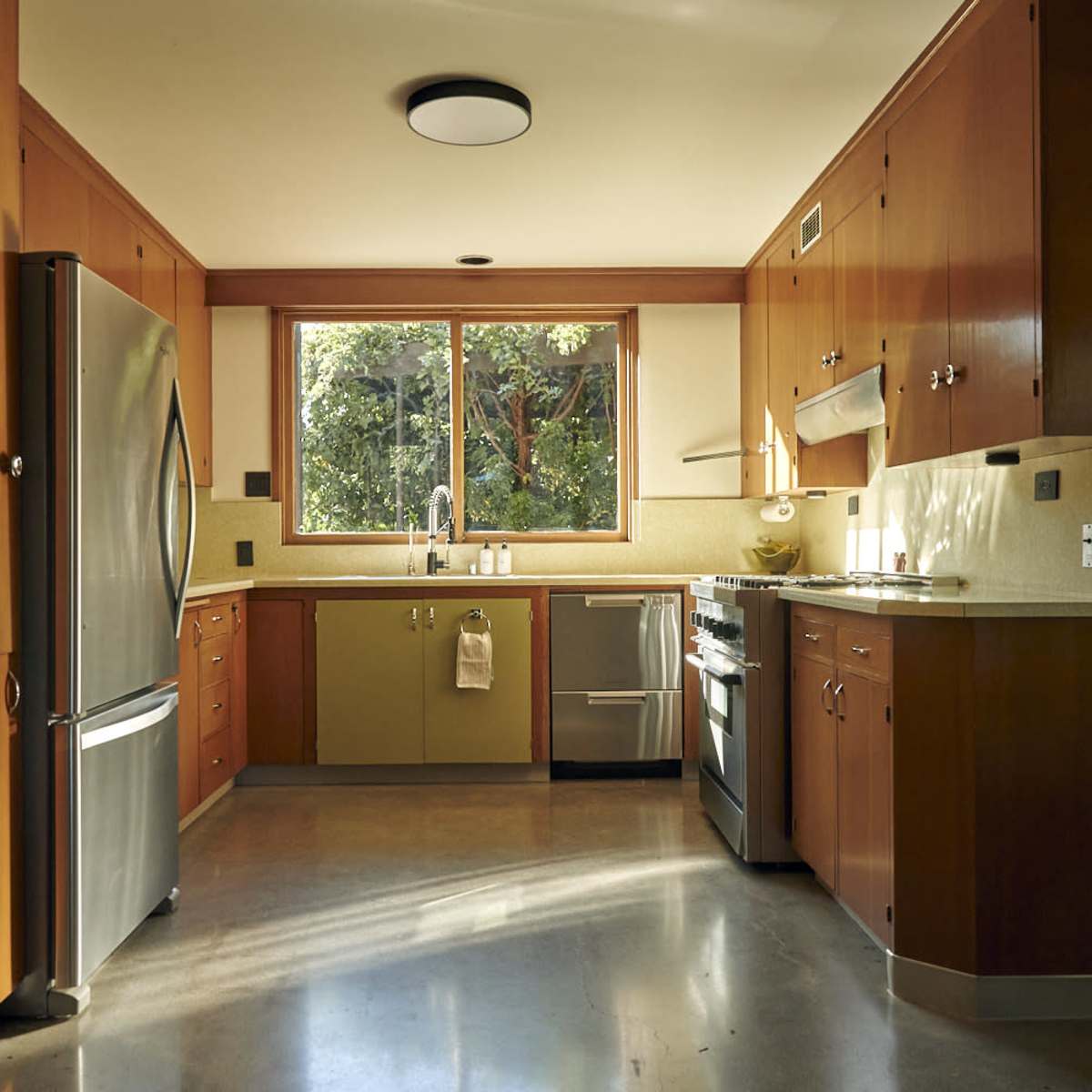 A modern kitchen with wooden cabinetry, stainless steel appliances, and a large window allowing natural light to enter.