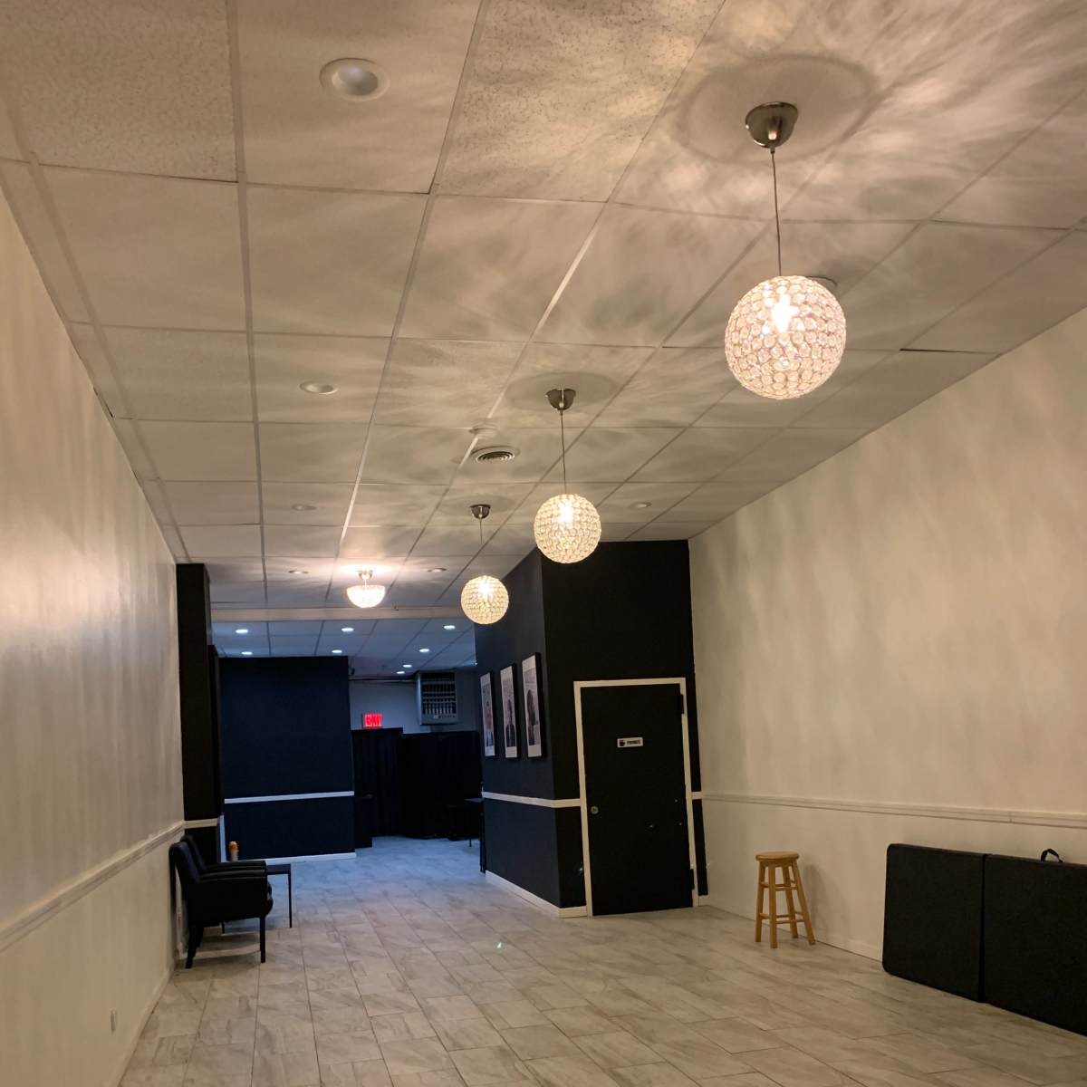 A hallway with tiled flooring, white walls, and decorative light fixtures hanging from the ceiling leads to a door at the far end.