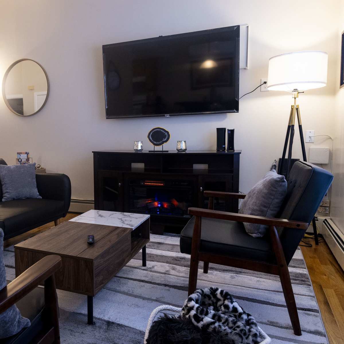 The living room features a black sofa with decorative pillows, a wooden coffee table, an electric fireplace, and a large television mounted on the wall.