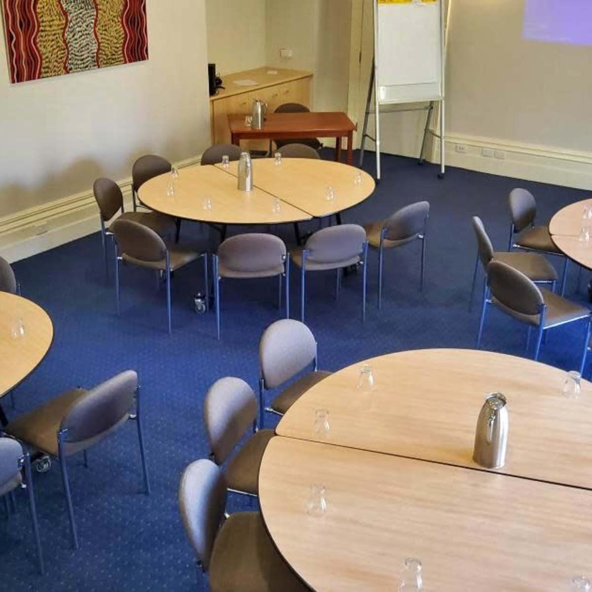 A conference room with several round tables arranged in a layout, each equipped with a water jug and glassware.