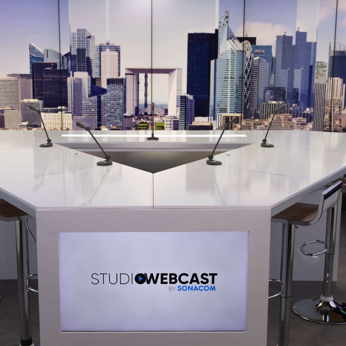A modern studio setup with a white table and several chairs, featuring a large city skyline backdrop.