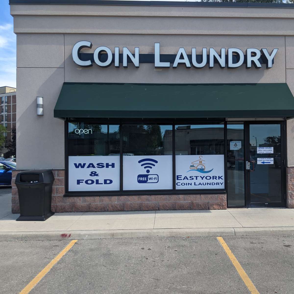 The exterior of a coin laundry facility with a green awning, featuring signs for wash and fold services and free Wi-Fi.