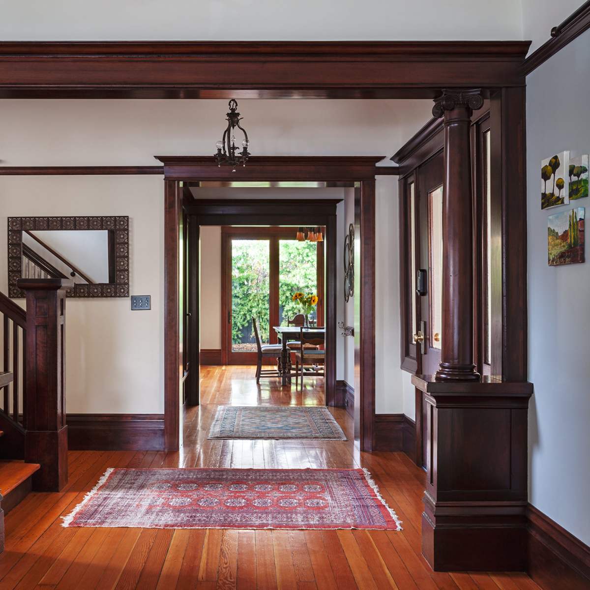 A spacious entryway with wooden columns, a staircase on the left, and a view into a dining area through an open doorway.