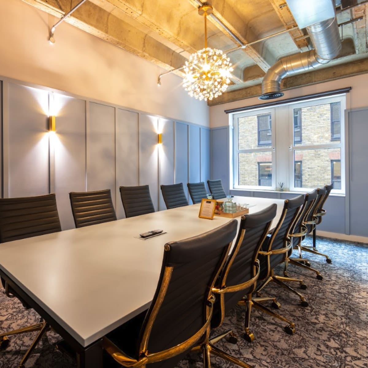 A modern conference room features a large table surrounded by black chairs, with decorative lighting and natural light streaming through a window.