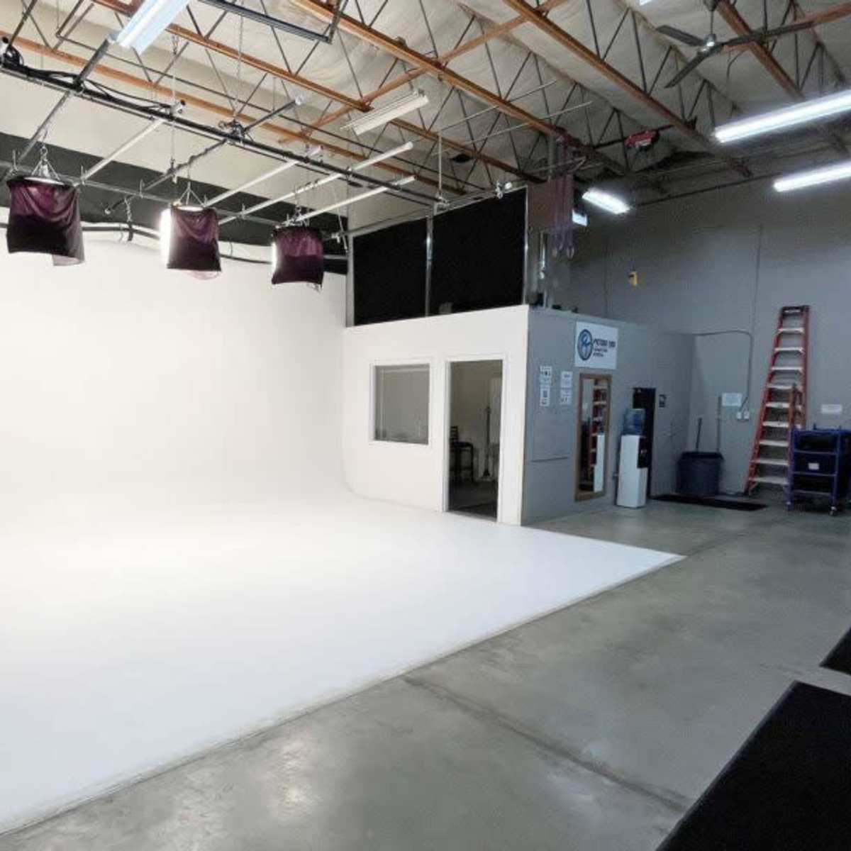 A spacious, empty photography studio with a white backdrop, overhead lighting, and storage areas along the walls.