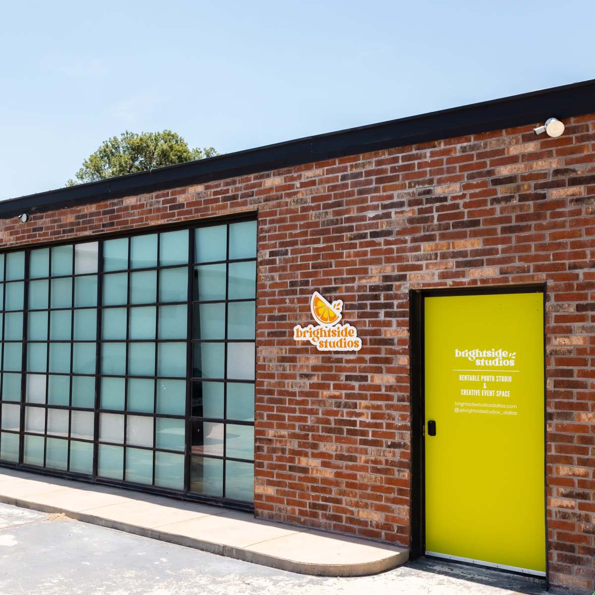 A brick building with large glass windows and a bright yellow door labeled "Brightside Studios."