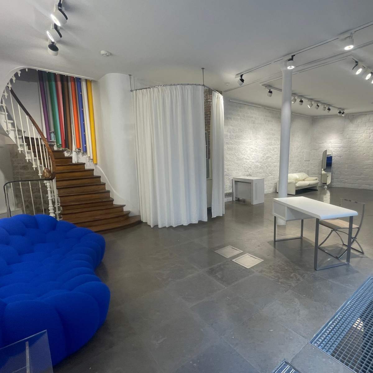 A spacious room with a blue couch, a white table, and colorful dividers leading up a staircase.