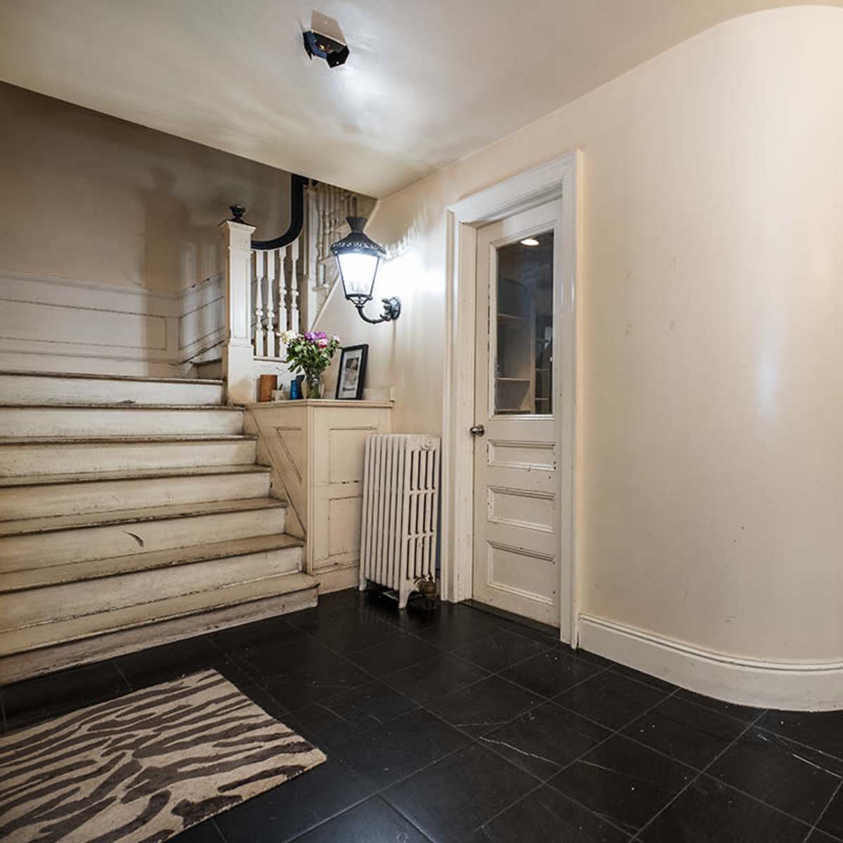 A hallway with a curved wall, a white staircase, a glass shower enclosure, and a door leading to another room.