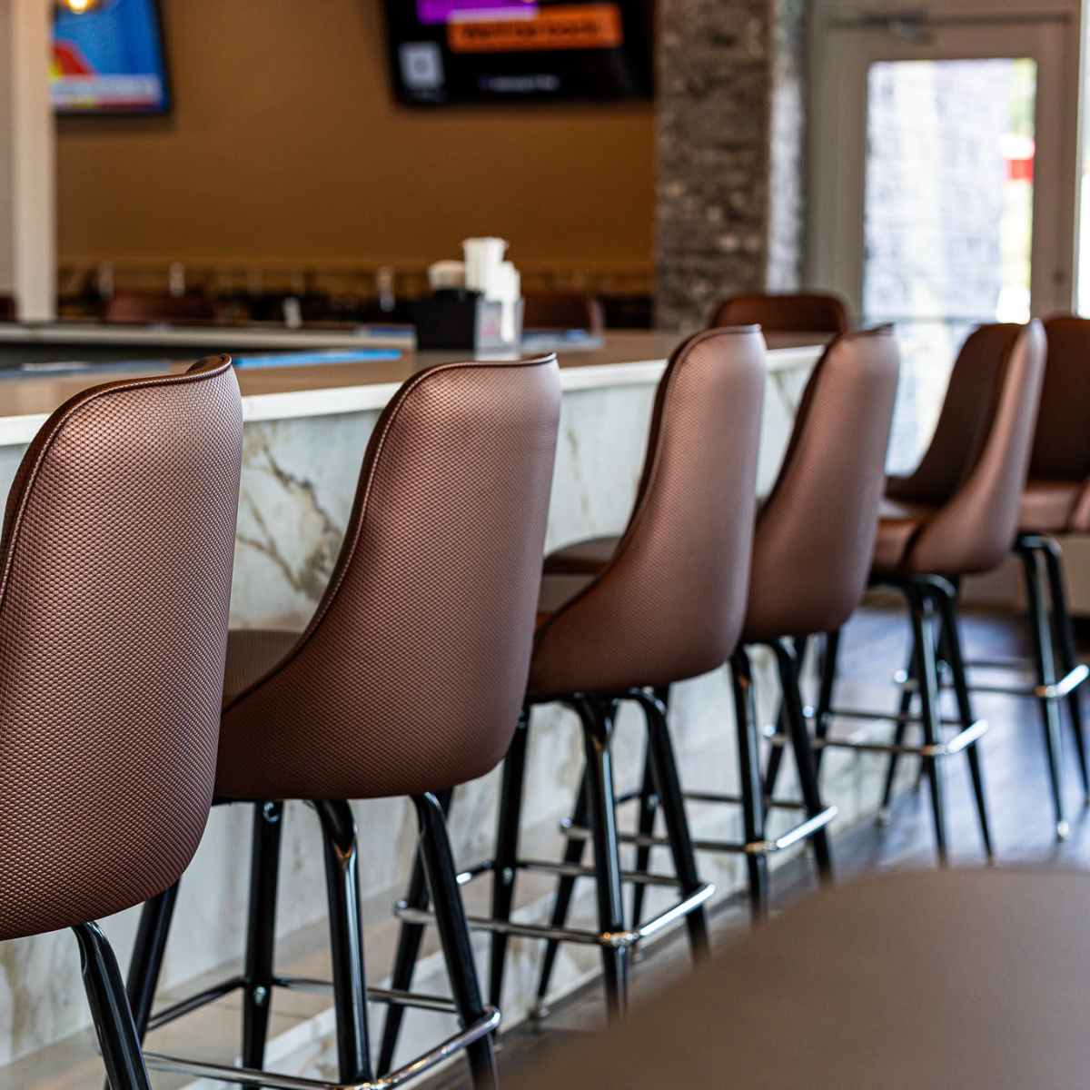 A row of brown leather bar stools positioned at a marble-topped counter in a casual dining space.