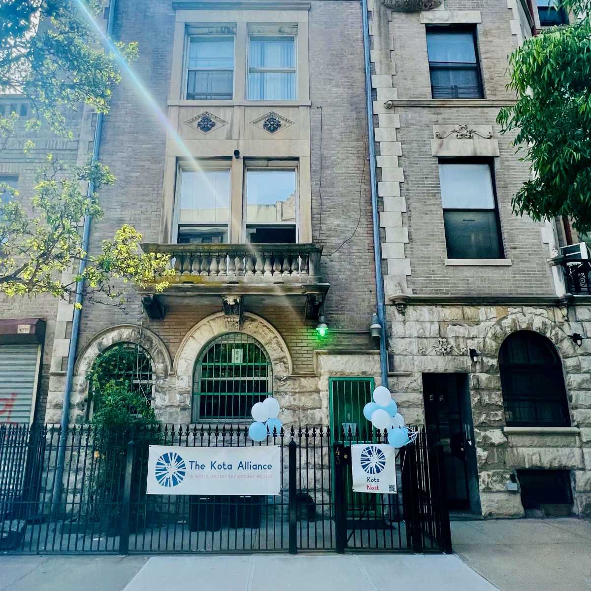 A multi-story brick building featuring architectural details like ornate windows and a balcony, with a banner for "The Keto Alliance" displayed outside along with blue balloons.