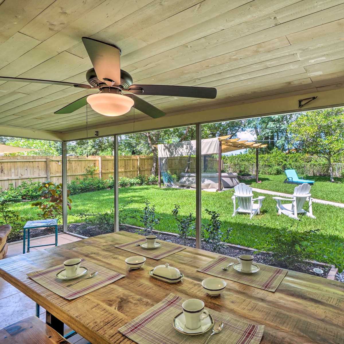 A spacious screened porch features a wooden dining table set with dishware, overlooking a green backyard with a lounge area and a gazebo.