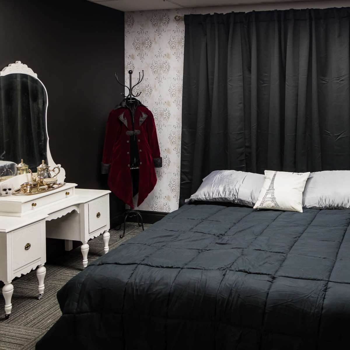 A neatly made bed with a dark comforter is positioned in a room featuring a black and white wallpapered wall, along with a large mirror and a white dresser.