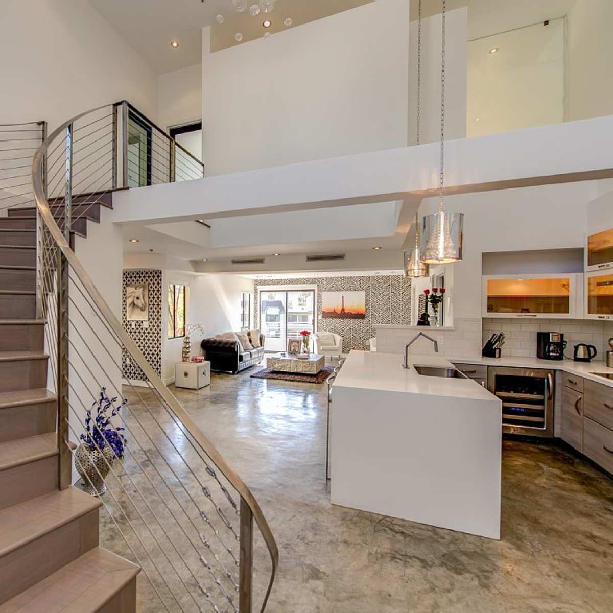 A modern open-concept living space features a spiral staircase, a sleek kitchen, and large windows allowing natural light to fill the area.