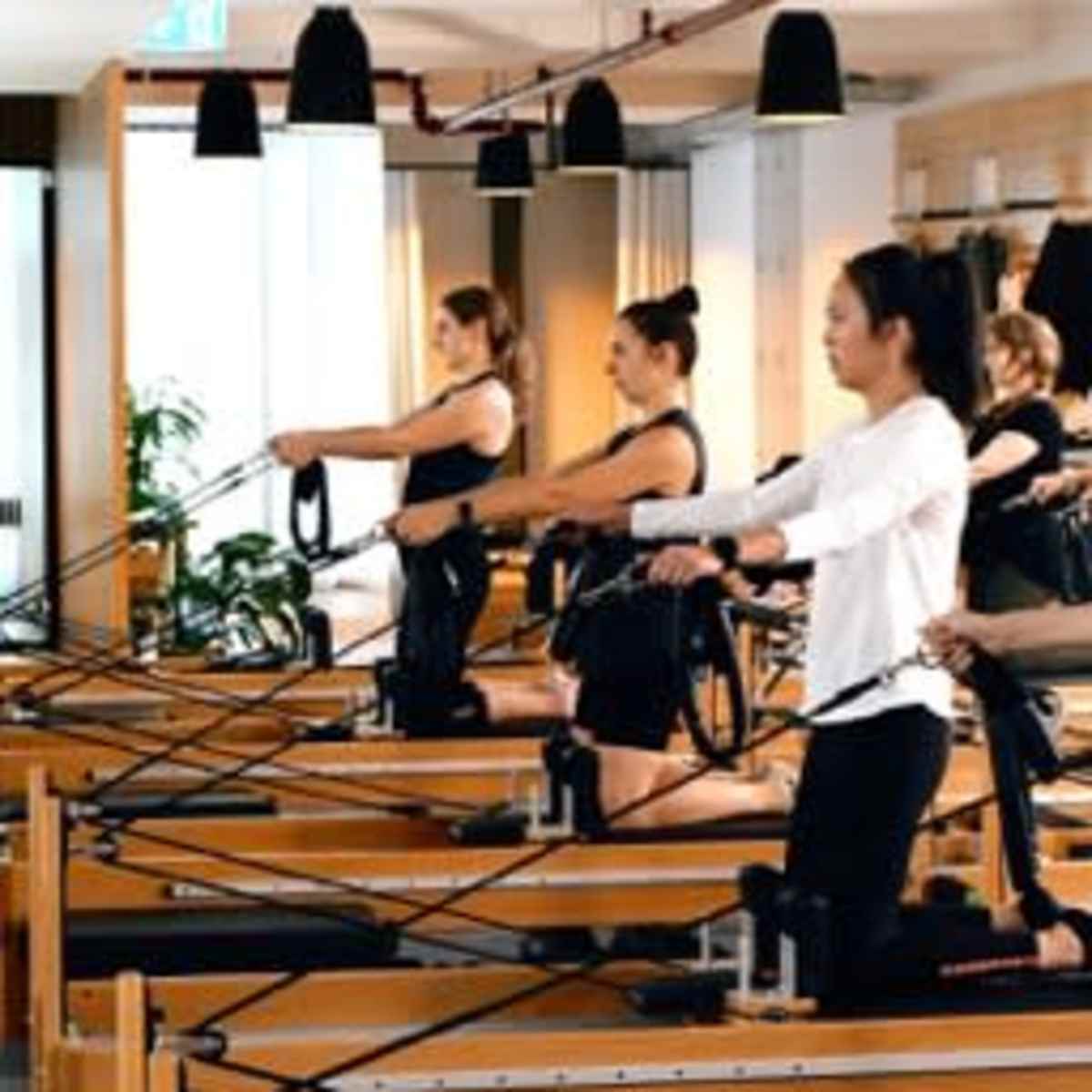 A group of individuals is performing exercises on reformer Pilates machines in a bright studio.