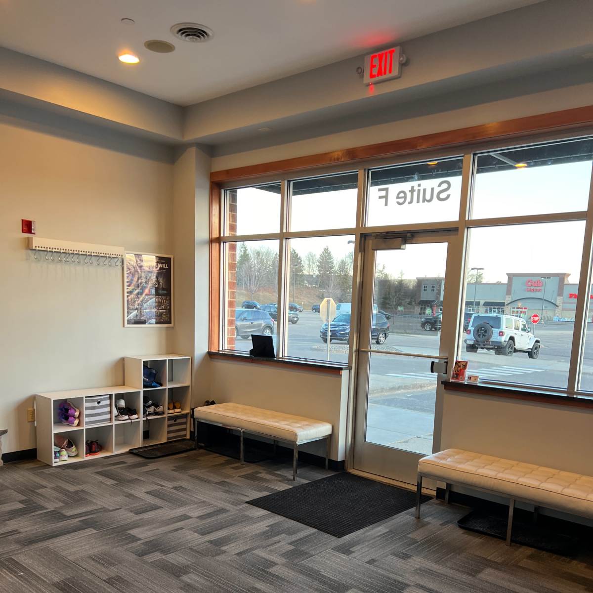 A spacious lobby area with a bench, shelving units, and large windows facing a parking lot.