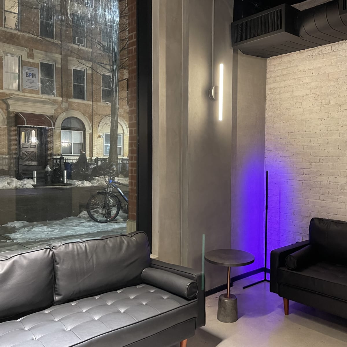 A modern interior with two black sofas facing a large window that reveals a snowy street and a bicycle outside.