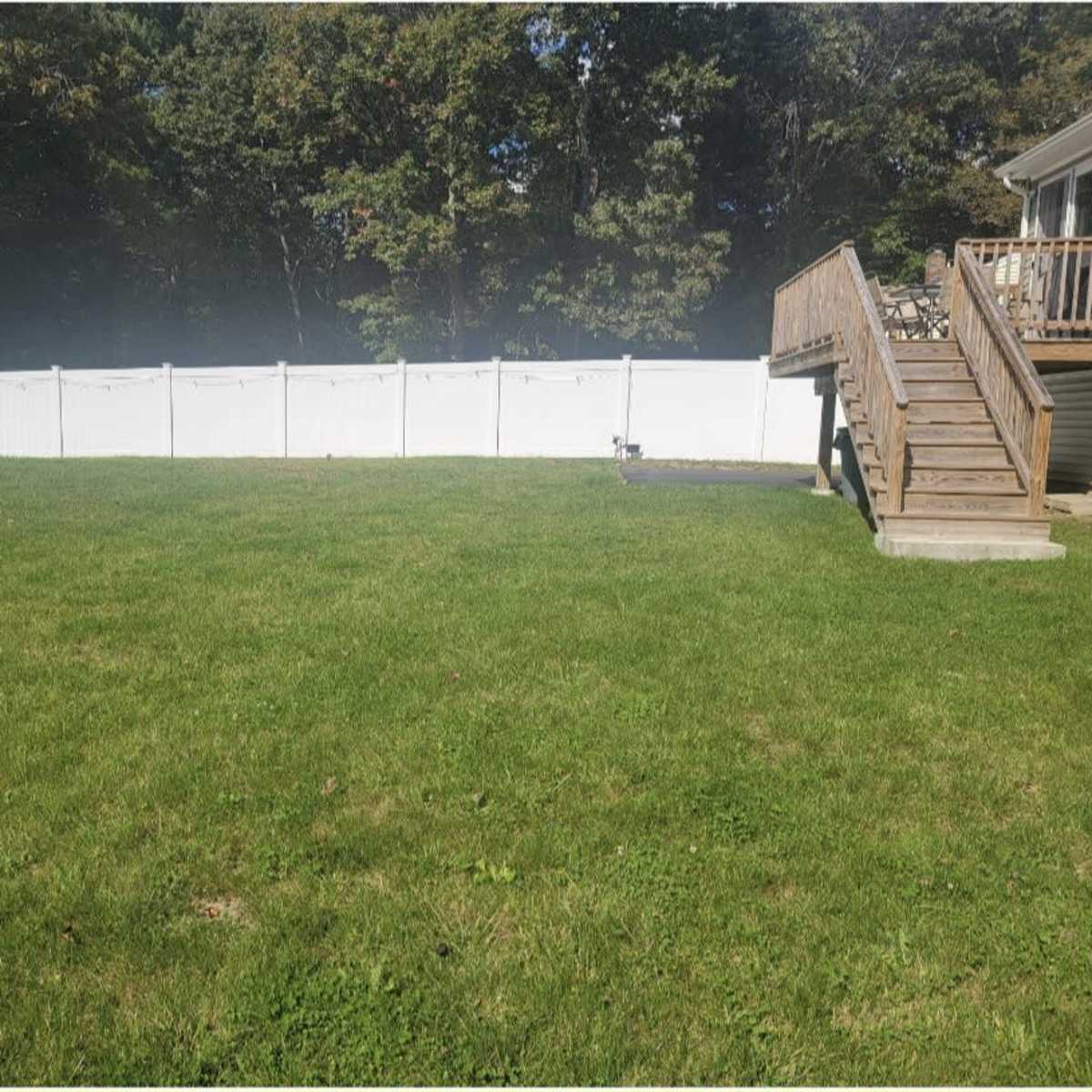 A grassy yard is enclosed by a white fence with a wooden deck visible to the right.
