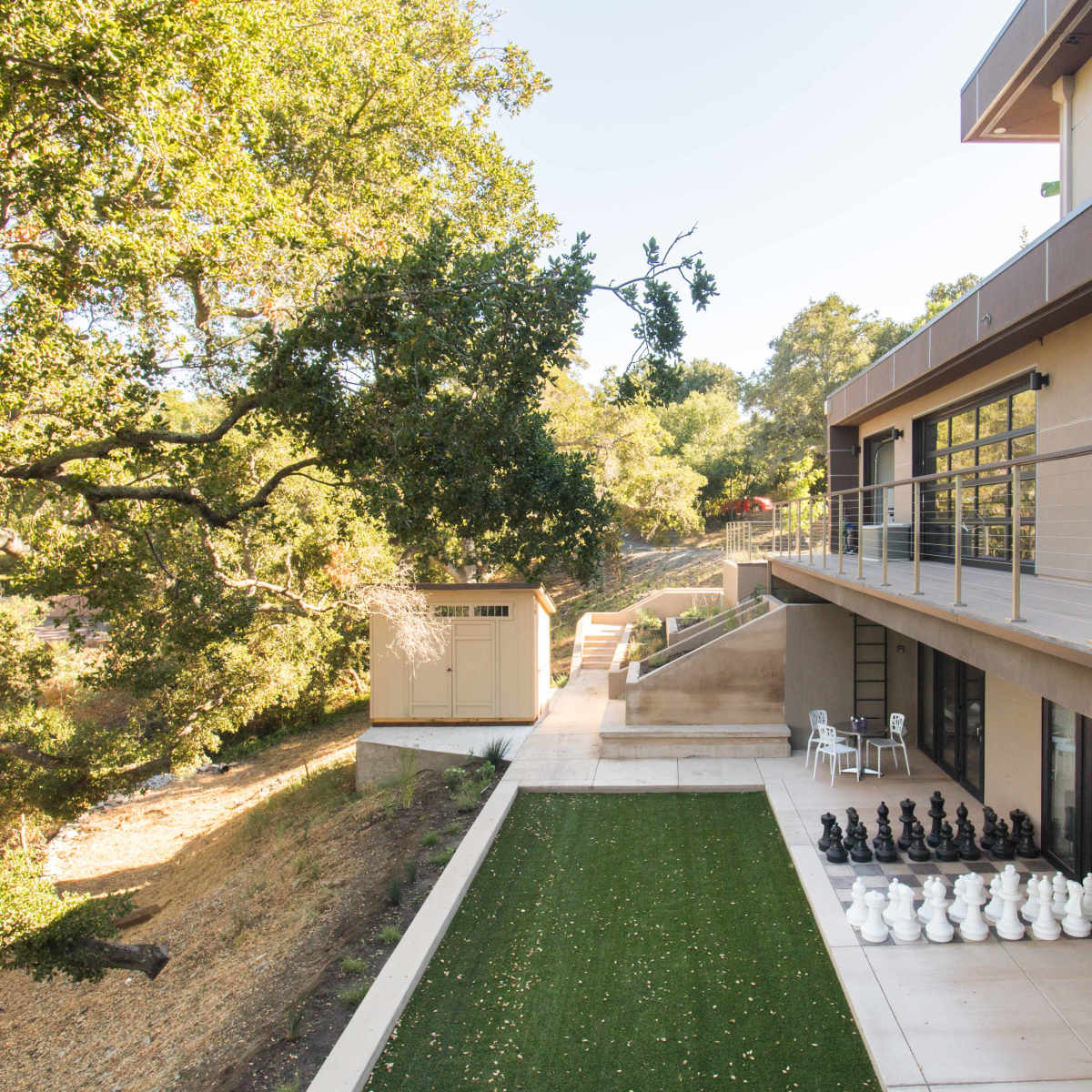 A modern two-story house with large windows, an outdoor terrace, and a landscaped area featuring a row of black and white chess pieces.