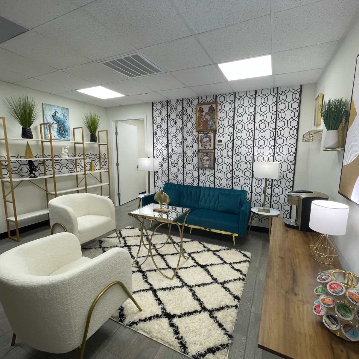 A modern office lounge area with teal and white furniture, geometric decor, and a patterned accent wall.
